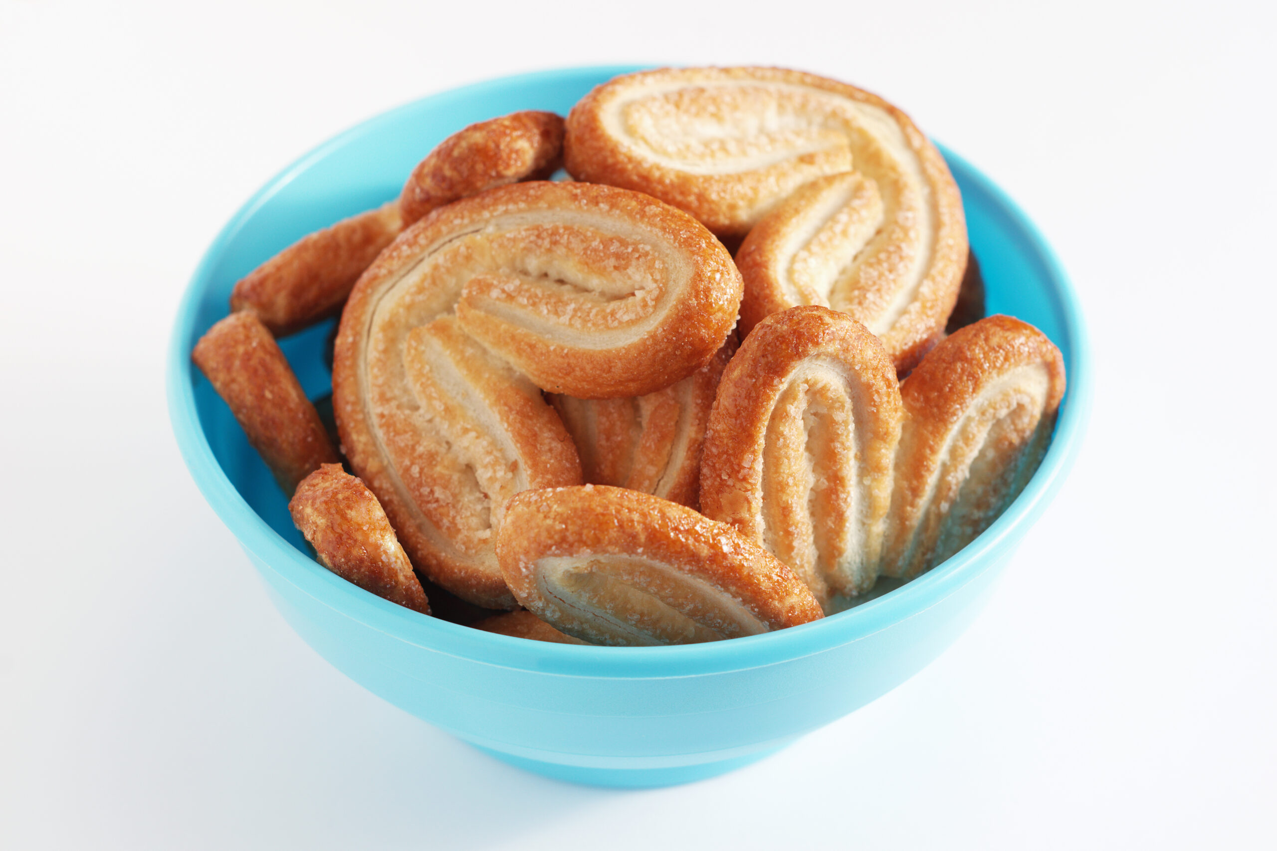 Palmiers puff pastry cookies in blue plastic bowl on a white background