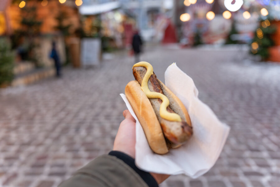 POV of unrecognizable man holding bun with sausage, at the Christmas market