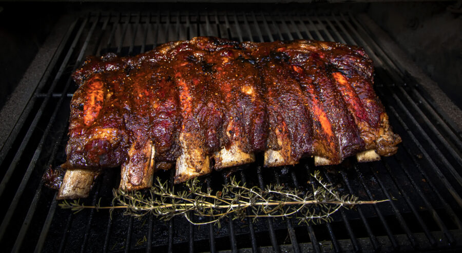 Rack of beef ribs cooking on a barbecue with a sprig of rosemary