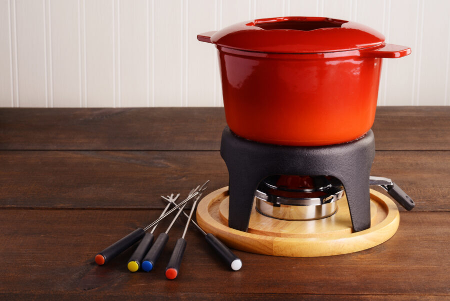 red cast iron fondue pot with skewers on wood table