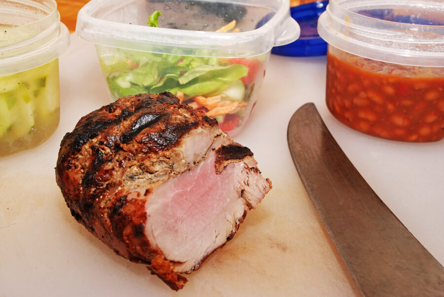 Slicing grilled tenderlon steak on cutting board surrounded by assorted leftovers -- baked beans, pickled cucumbers and garden salad.