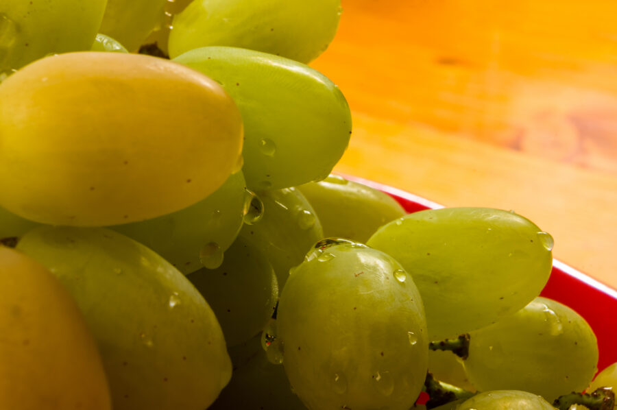 a large brush of green grapes with water drops in a red ceramic plate on a wooden background