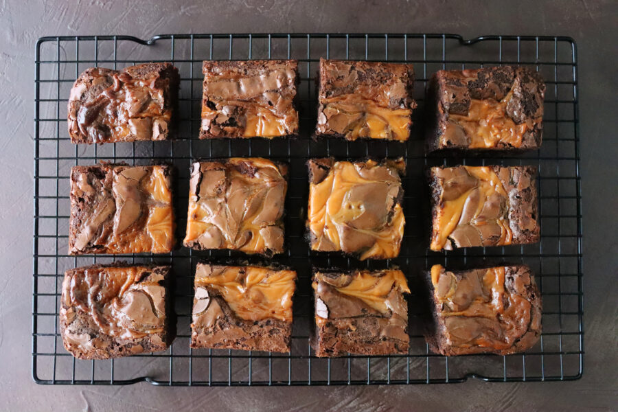 Stock photo showing elevated view of cooling rack of homemade chocolate salted caramel brownies cut into square slices.