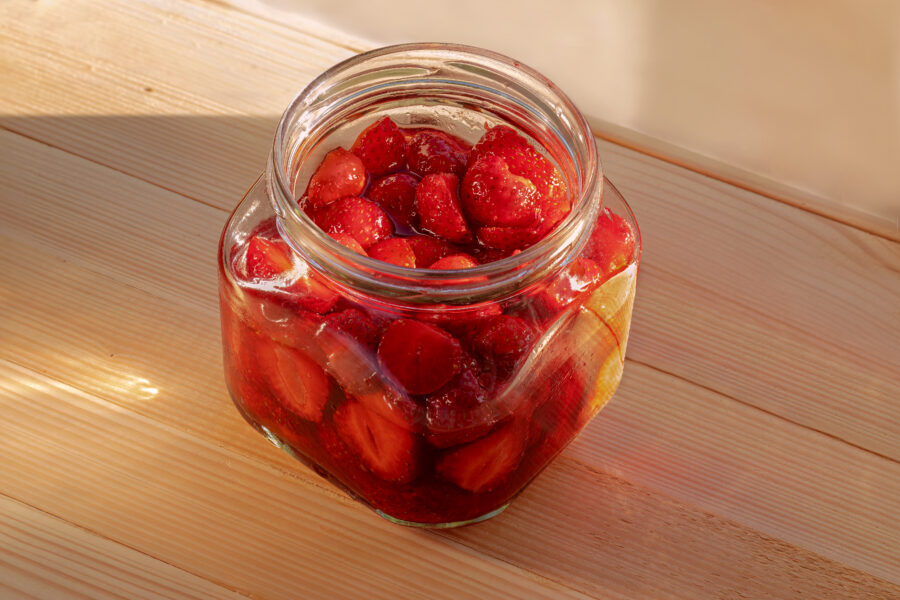 Strawberries cut into halves in glass jar in honey