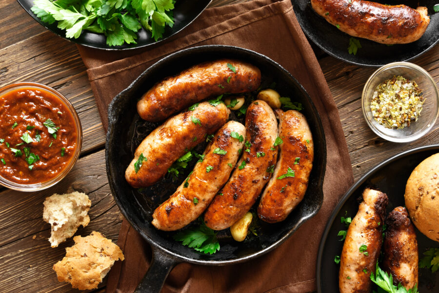 Tasty fried sausages in frying pan over wooden background. Top view, flat lay