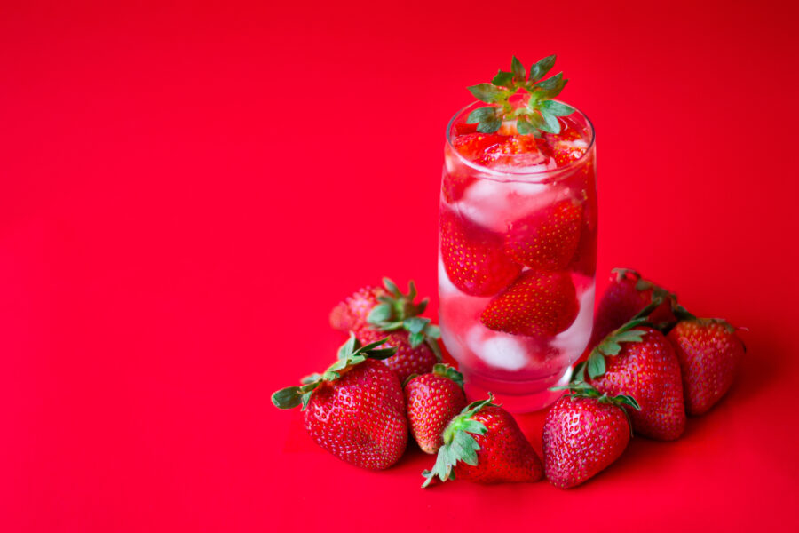 This image features a Refreshing Strawberry Cocktail with Ice set against a vibrant red background. 