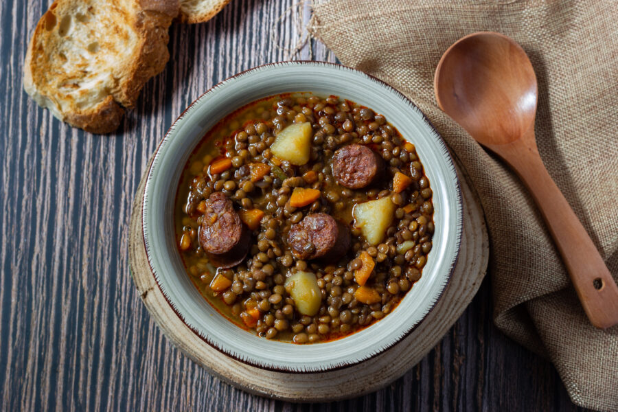 Traditional lentil soup with legs, carrots and chorizo sausage on a wooden background and rustic spoon.