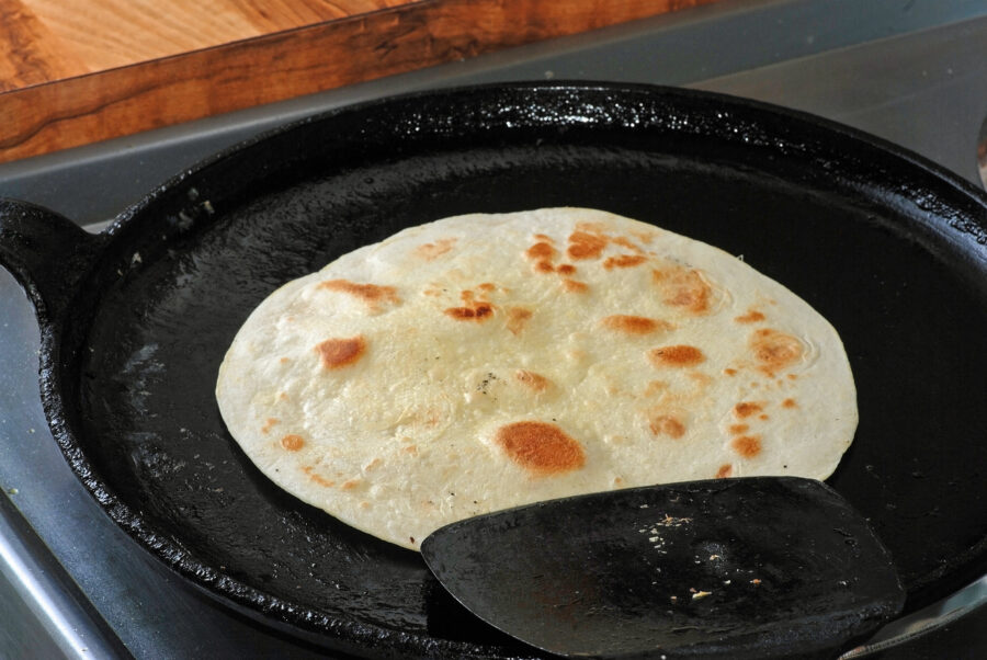 Browning tortilla in cast iron comal skillet in preparation for burrito ingredients.