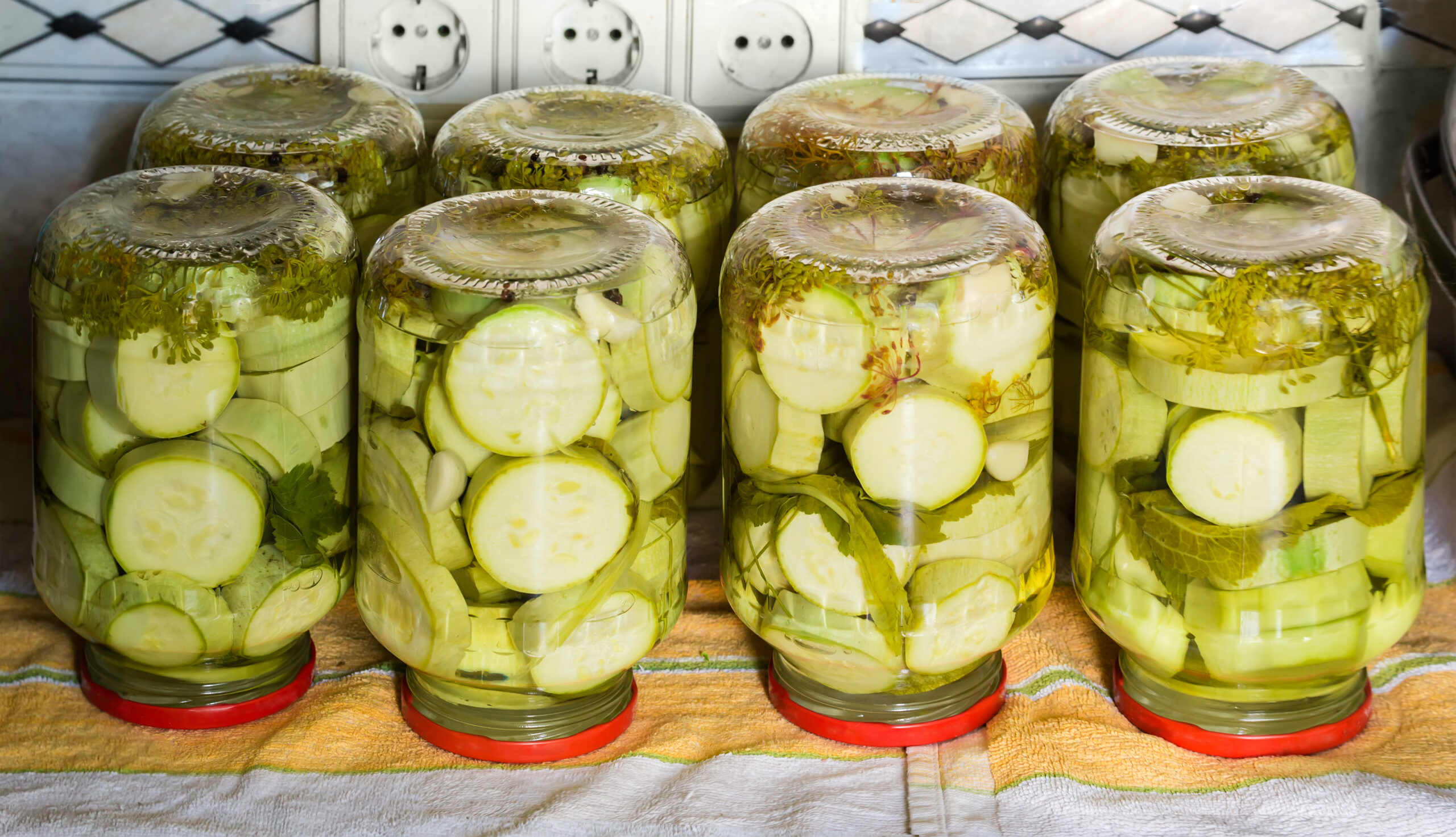 Canned vegetable marrow cut into circles with spices in the glass jars turned upside down on a napkin on kitchen table during the home canning