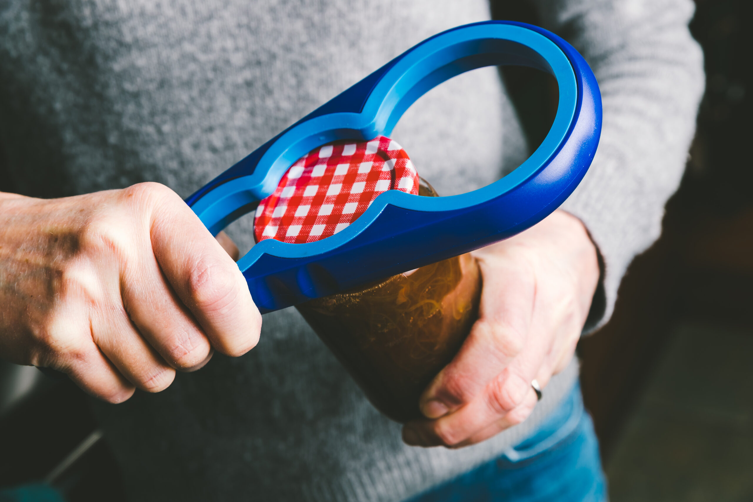 Woman using a plastic gripper to rotate the lid off a tightly fitting jar of gooseberry jam.