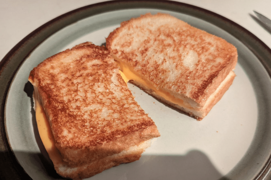 Golden-brown grilled cheese sandwich cut in half and served on a ceramic plate, with melted orange cheese oozing slightly from between the toasted slices of bread.