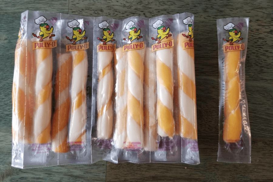A row of individually wrapped Polly-O twist cheese sticks, featuring a swirl of white mozzarella and orange cheddar cheese. The packaging shows a cartoon chef character, and one stick on the far right is shorter than the rest.