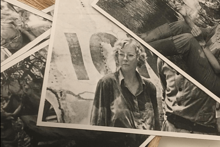 A close-up of several overlapping black-and-white photographs spread out on a table, with the central image featuring a woman in glasses and a button-up shirt standing in front of a weathered airplane fuselage. Other partial images show scenes of jungle exploration and aircraft wreckage.