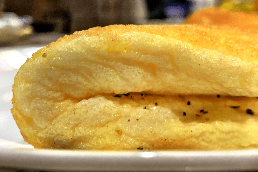 Close-up of a fluffy, golden-yellow omelet with a soft, airy texture and visible folds, lightly seasoned with black pepper. The omelet sits on a white plate, highlighting its light and pillowy interior.