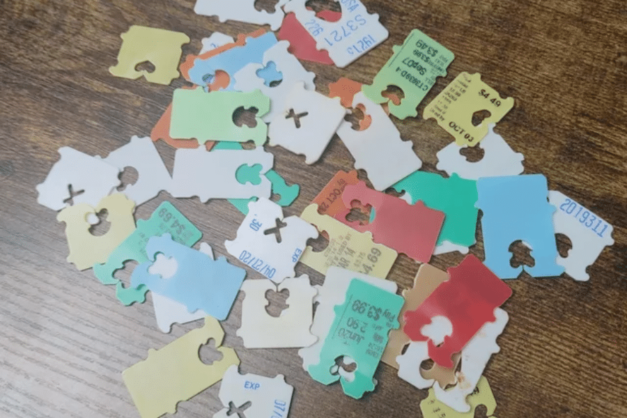 A scattered collection of colorful plastic bread clips on a wooden surface, commonly used to seal bags of bread and often printed with expiration dates or product codes.