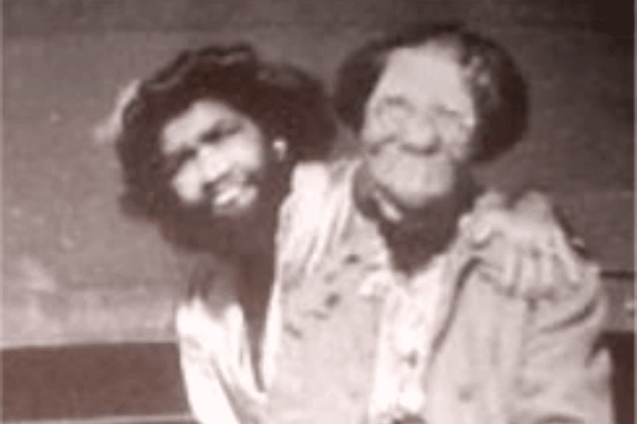 Grainy black and white photograph of two women with rare physical conditions seated side by side, one with hypertrichosis (excessive facial hair, often referred to historically as the "bearded lady") and the other with significant facial deformities. They are smiling and embracing, conveying warmth, solidarity, and shared experience despite the exploitative environments many such individuals were placed in during the sideshow era.
