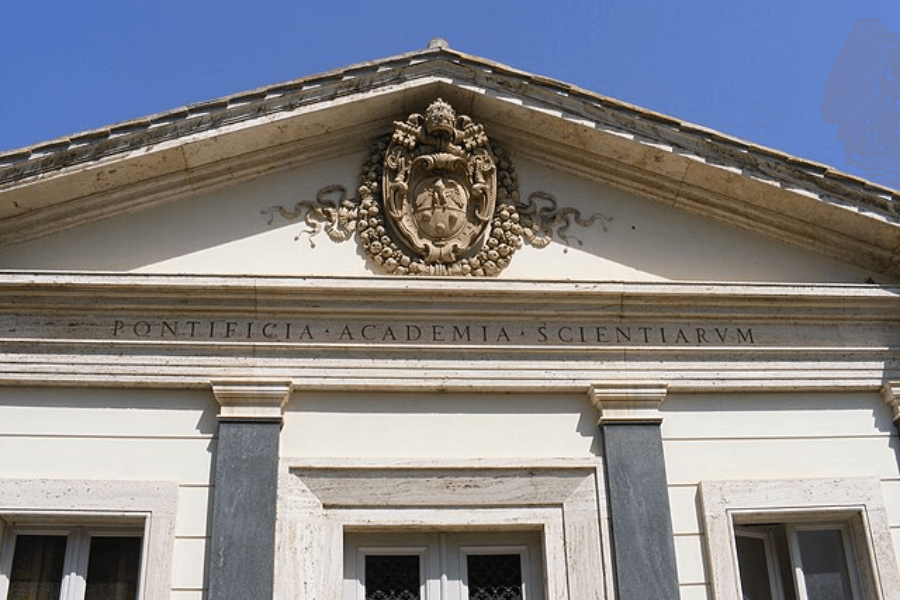 Facade of the Pontifical Academy of Sciences building in Vatican City, featuring a Latin inscription “PONTIFICIA ACADEMIA SCIENTIARUM” below a triangular pediment adorned with a sculpted papal coat of arms and decorative garlands.