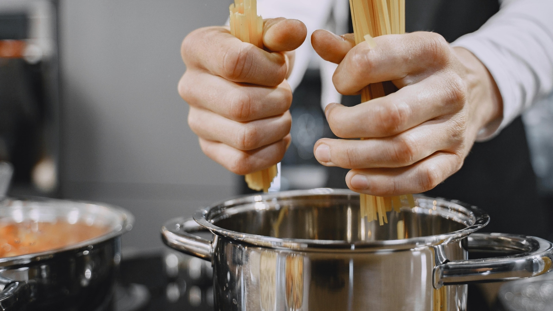 Hand placing spaghetti into a stainless steel pot on a stove
