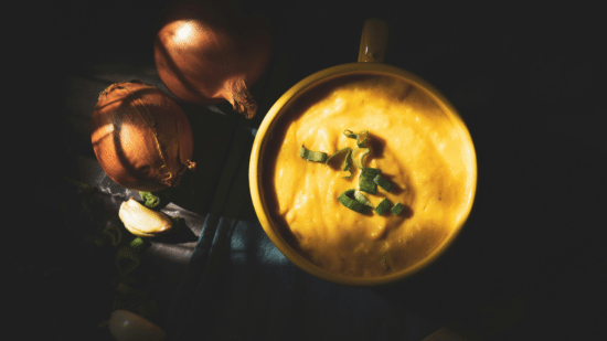 Man holding a stainless steel bowl filled with soup in a kitchen