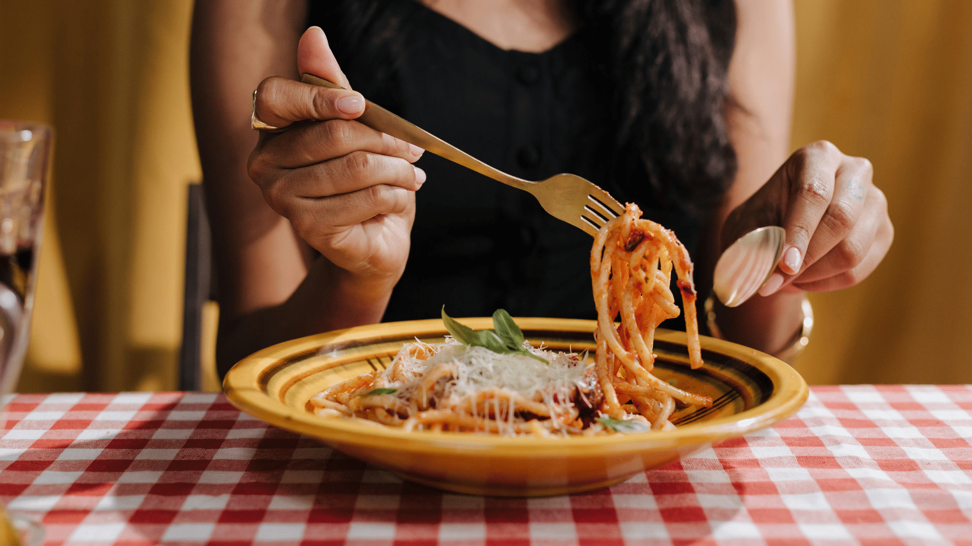 Woman holding a fork with cheesy pasta above a plate in a warmly lit kitchen