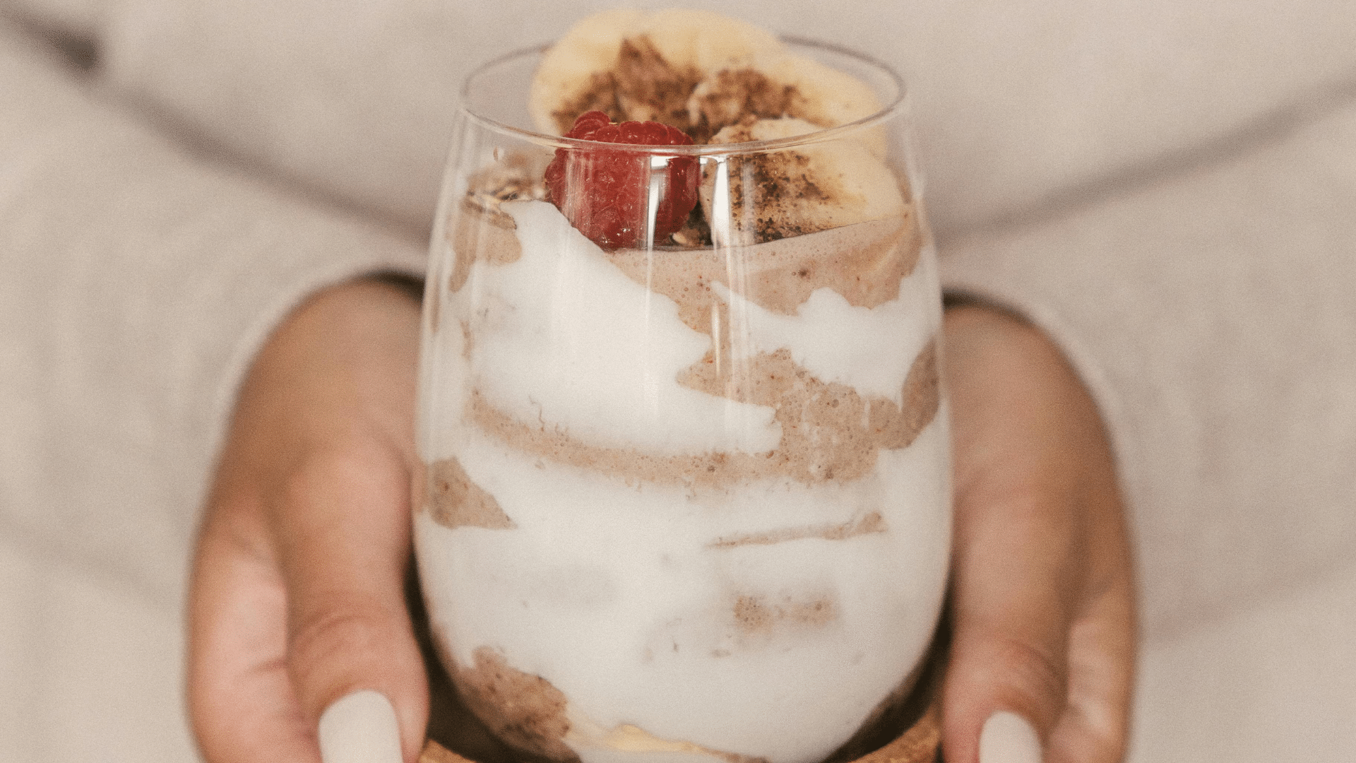 Person holding a smoothie drink with fruit toppings.