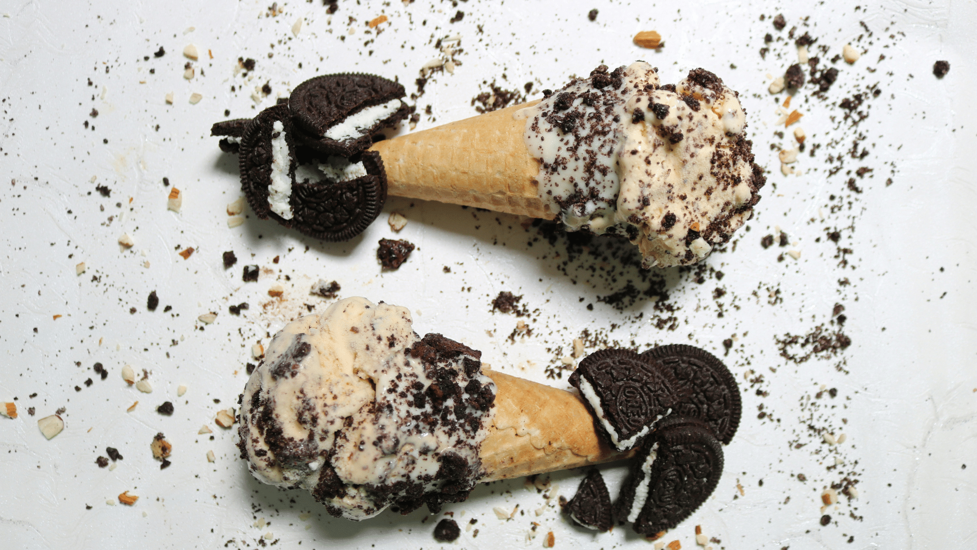 Two ice cream cones topped with crushed Oreo cookies