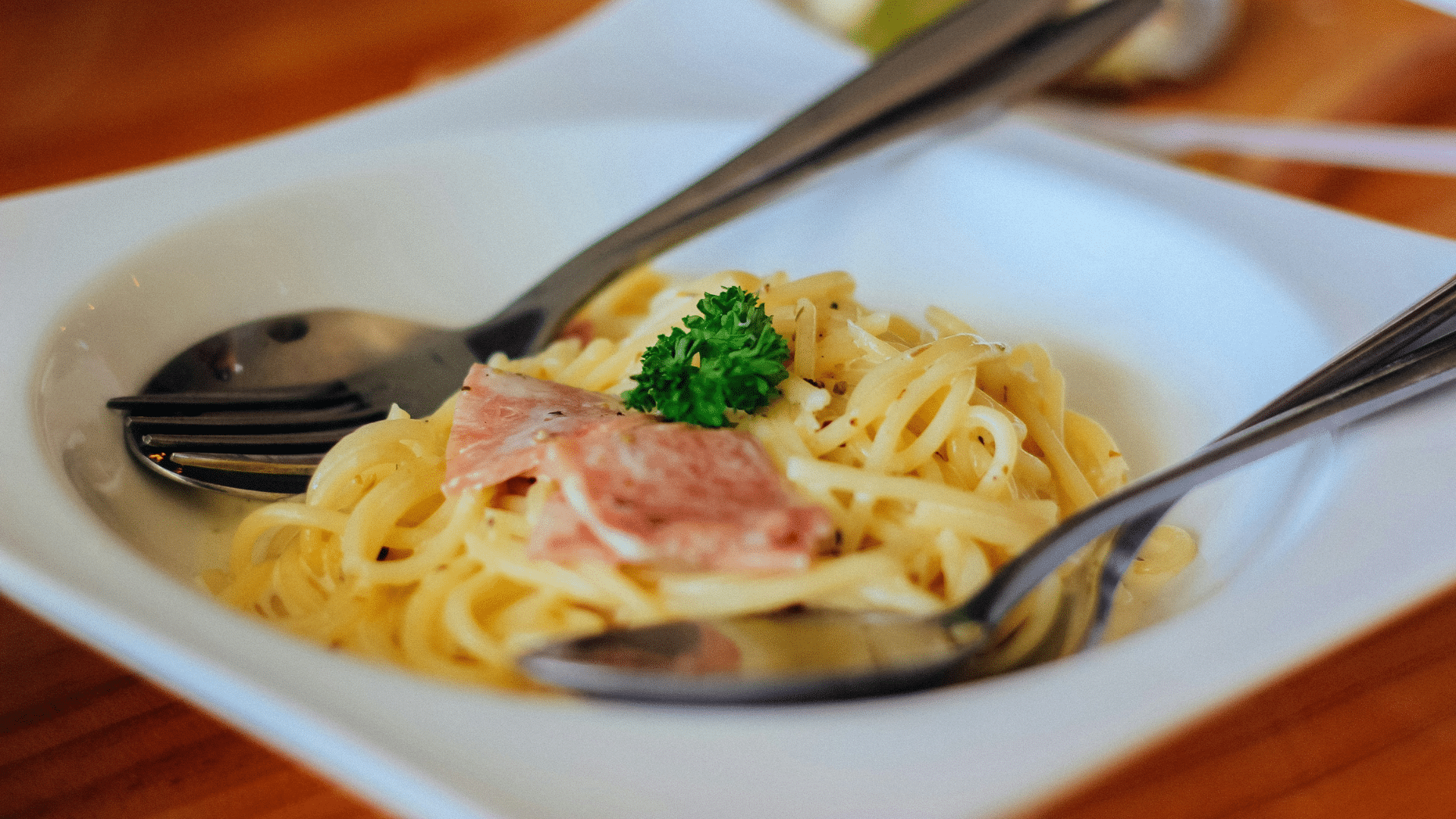 Chicken carbonara pasta in a white plate with creamy cheese sauce and herbs
