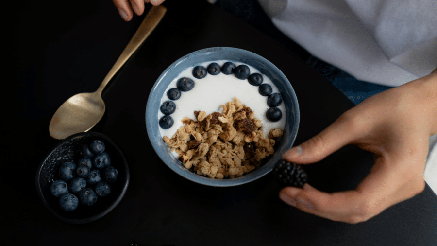 Bowl filled with granola, milk, and blueberries on a dark surface