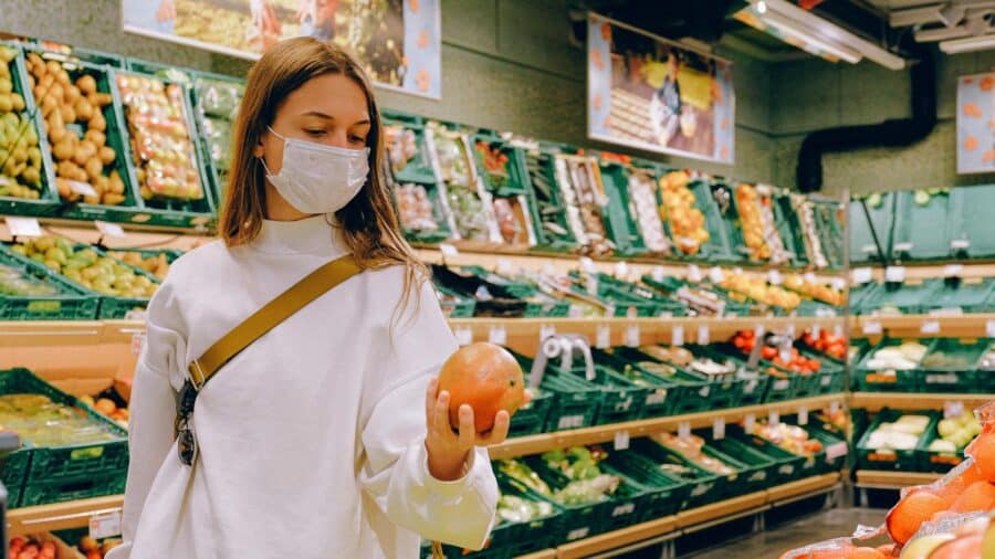 Woman wearing a mask and pushing a shopping cart through a grocery aisle