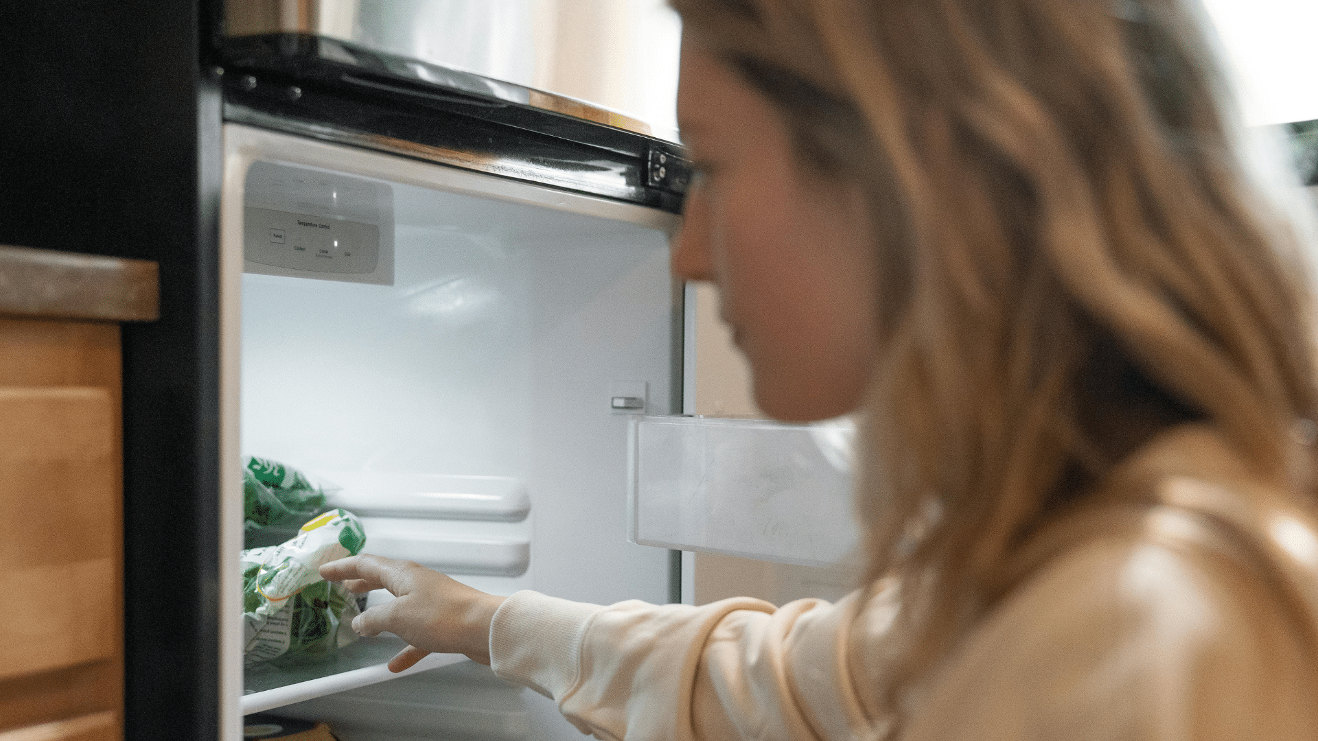 Woman in a brown shirt looking inside an open refrigerator