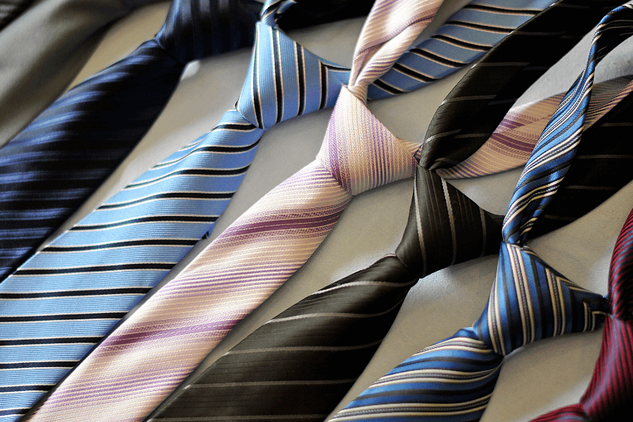 This image shows an assortment of neatly arranged neckties with various colors and striped patterns. The ties, which include shades of blue, pink, and black, are knotted and laid out on a flat surface, suggesting a display or preparation for use.