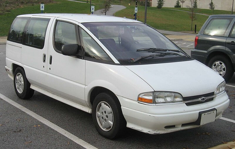A white Chevrolet Lumina APV minivan parked in a lot with accessible parking spaces nearby. The van has a rounded, futuristic design typical of 1990s minivans, with large side windows and a sliding door on one side.