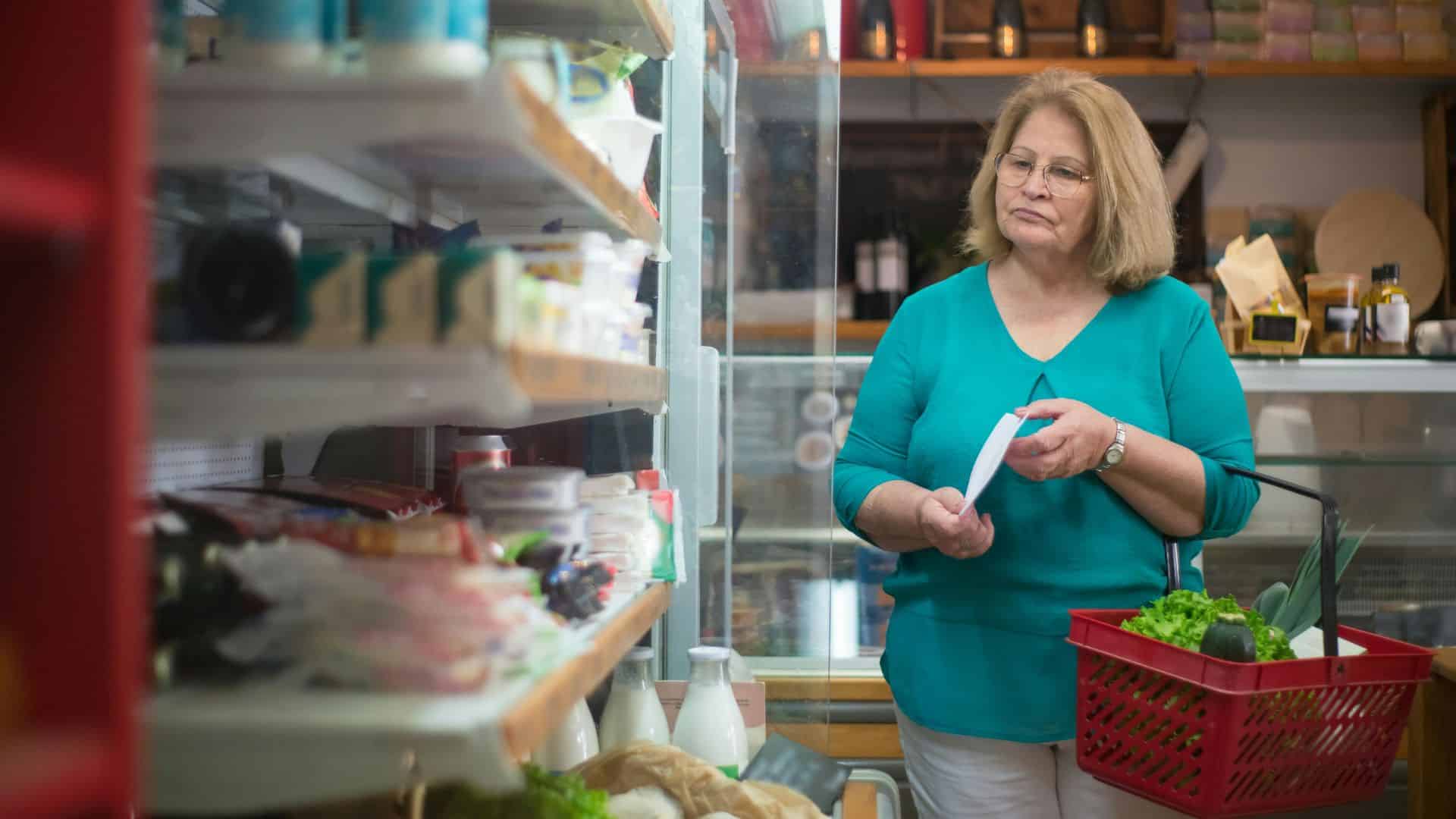 Elderly woman looking at a grocery list while shopping in a supermarket