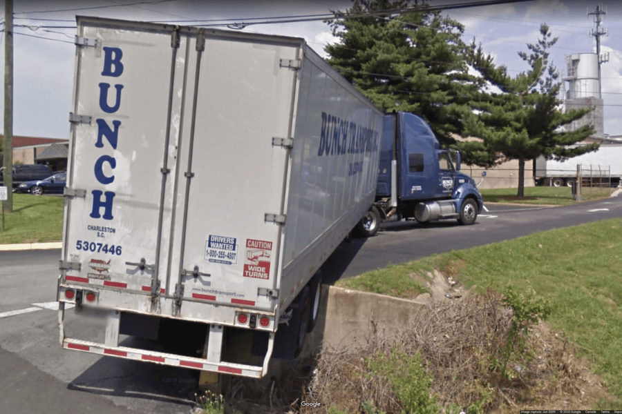 This image shows a large semi-truck with the logo "BUNCH" on its trailer, partially off the road with the back end of the trailer hanging over a ditch or drainage area. It appears as though the truck either misjudged a turn or attempted to back up and ended up in an awkward, potentially hazardous position.