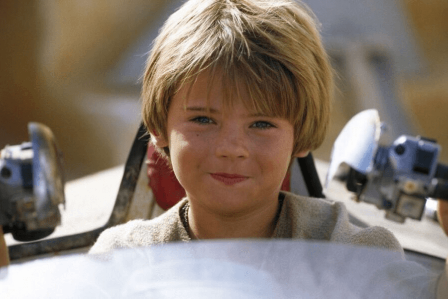 This image features a young boy with short, light brown hair and a cheerful expression, sitting in what appears to be a futuristic or mechanical vehicle. The background is blurred, emphasizing the boy and the vehicle controls, creating a sense of adventure or curiosity.