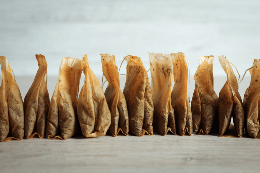 This image shows a row of used tea bags neatly lined up on a wooden surface. The tea bags are stained with rich brown tones from steeping, emphasizing their spent state. The neutral background creates a simple and rustic aesthetic.