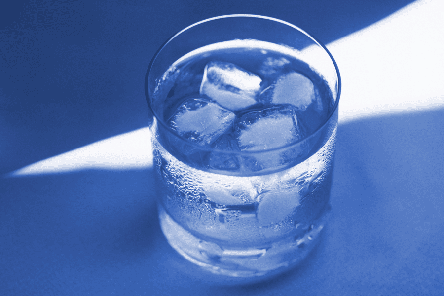 A close-up of a glass filled with ice water, with condensation forming on the outside. The image has a cool blue tone, emphasizing the refreshing and chilled nature of the drink.