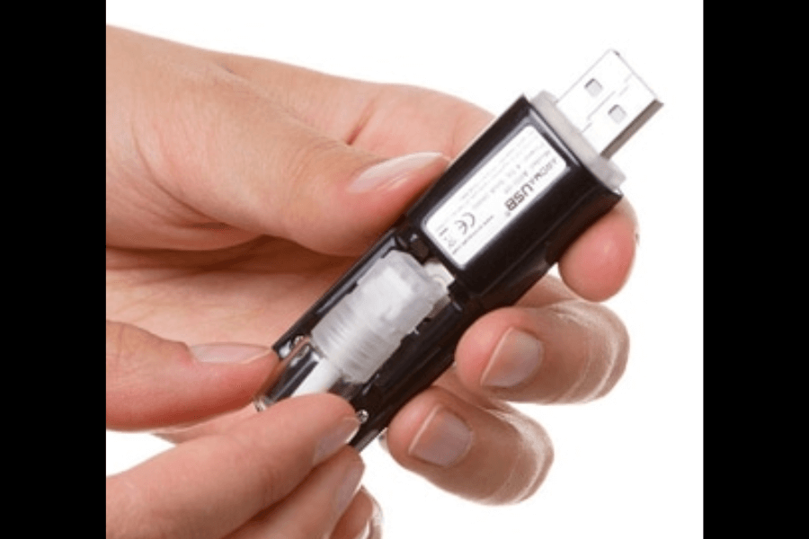 This image shows a close-up of hands holding a USB device that appears to have a removable compartment containing a small component, such as a liquid or specialized cartridge. The device is labeled with text, and its design suggests it may serve a specific function beyond standard data storage.