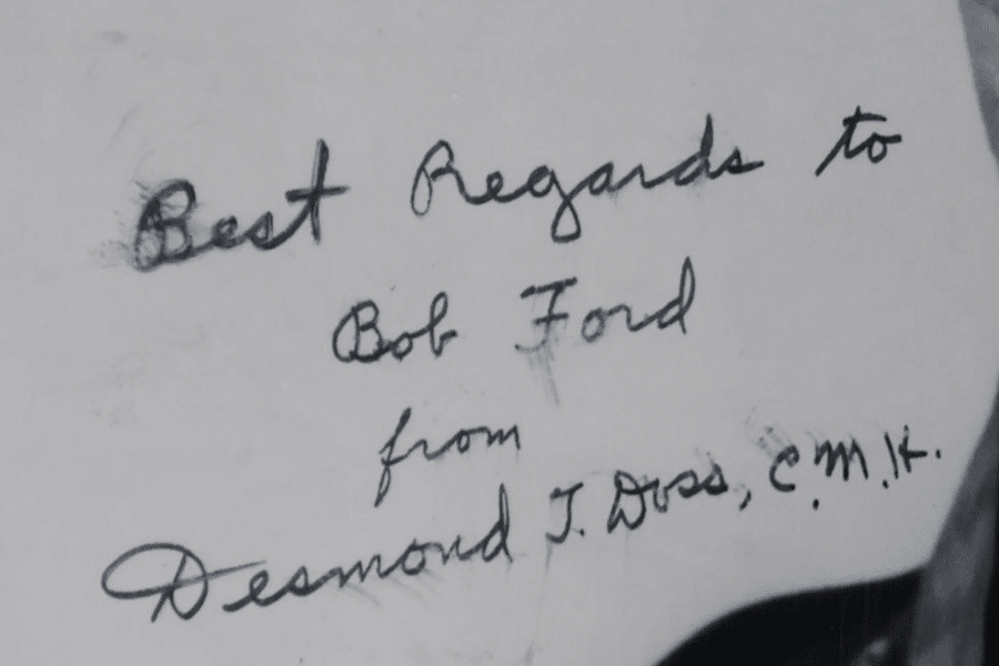Close-up image of a handwritten note that reads: “Best Regards to Bob Ford from Desmond T. Doss, C.M.H.” The message is written in cursive with black ink on white paper, and the signature belongs to Medal of Honor recipient Desmond Doss.