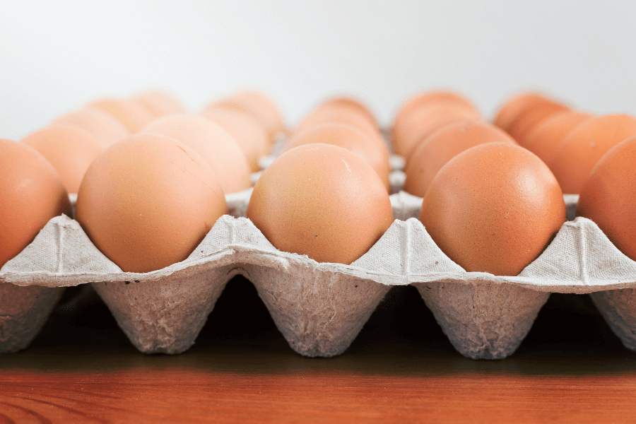 This image shows a carton of brown eggs neatly arranged in rows, placed on a wooden surface. The eggs have smooth shells, and the light, neutral background emphasizes their natural color and texture.