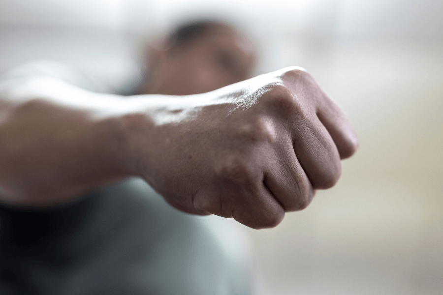 Close-up of a clenched fist extended outward, with a blurred person in the background, creating a powerful visual of anger, aggression, or confrontation.