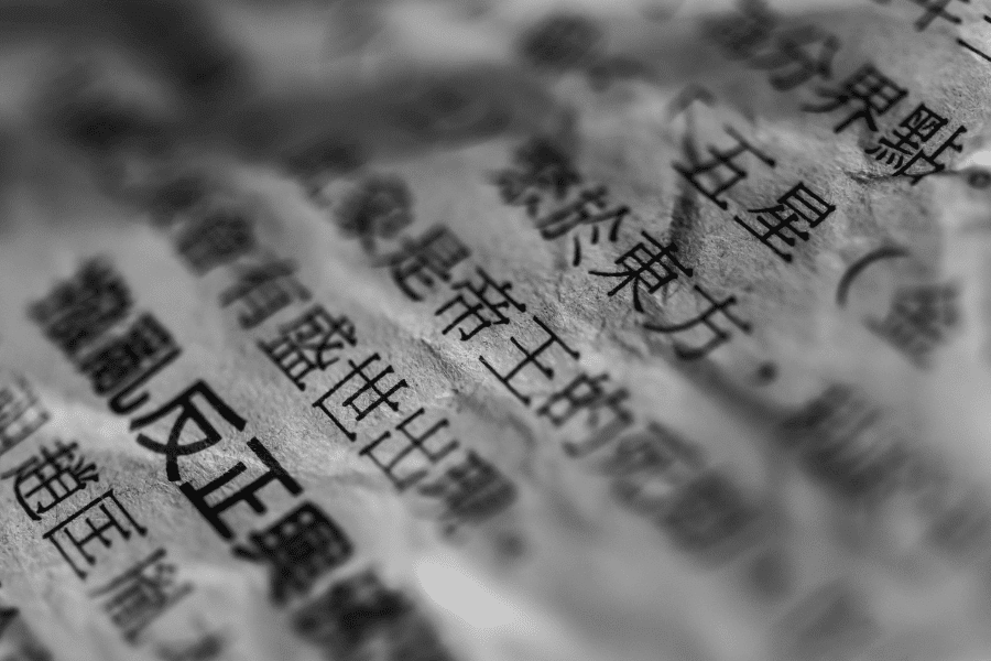 This black-and-white close-up image shows crinkled paper with printed text in Chinese characters. The textured surface and selective focus create a dramatic, artistic effect, highlighting the intricate details of the script.