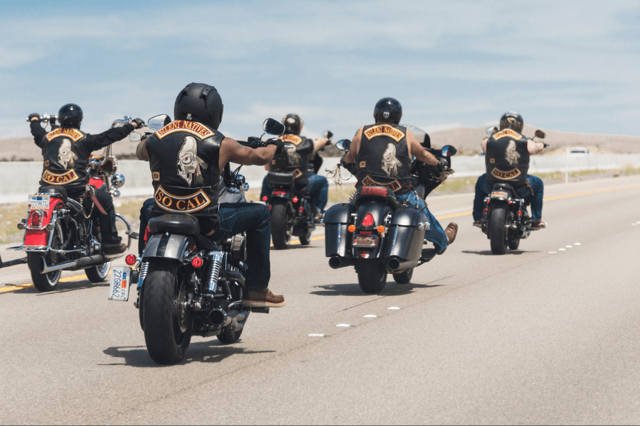 Group of motorcyclists riding down a highway, all wearing leather vests with "Silent Natives" and "So Cal" patches, showcasing a biker club on a scenic road trip under clear skies.