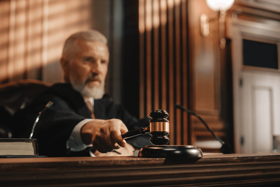 Older male judge in a black robe striking a gavel in a wood-paneled courtroom, signaling a formal decision or conclusion of legal proceedings.