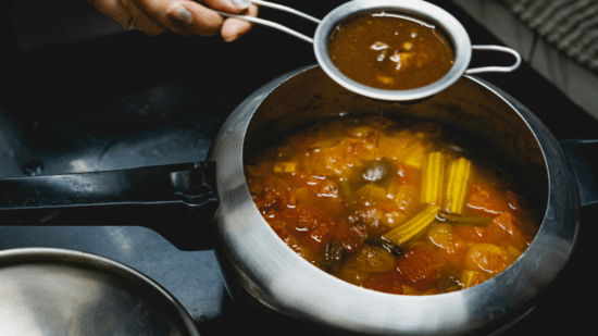 Person holding a spoon over a large pot of soup while cooking