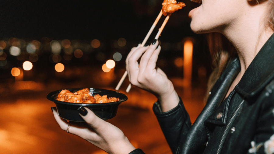 Close-up of a woman using chopsticks to eat meat with orange sauce
