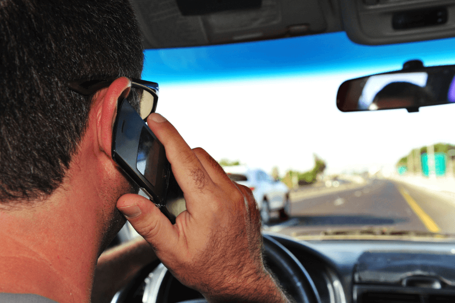 Close-up of a man driving on a highway while holding a smartphone to his ear, highlighting the dangerous act of distracted driving.
