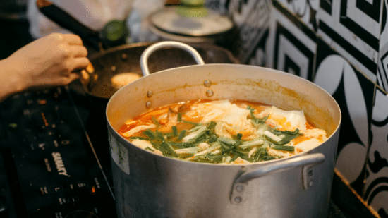 Pot of soup or stew simmering on a stove burner with herbs on top