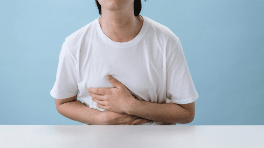 Man in a white t-shirt holding his stomach in discomfort