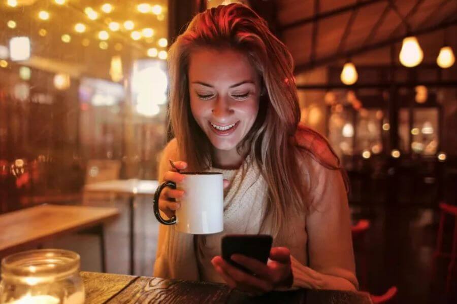 woman holding a mug while looking at their phone